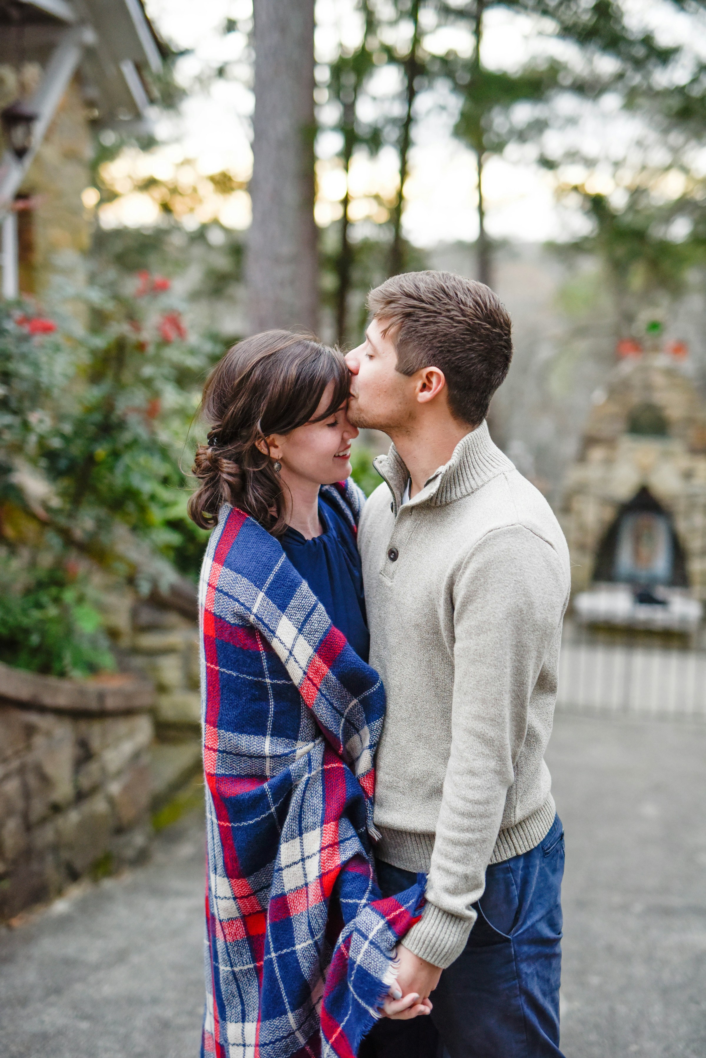 O casal abraçado sob uma manta xadrez, ele beijando a testa dela
